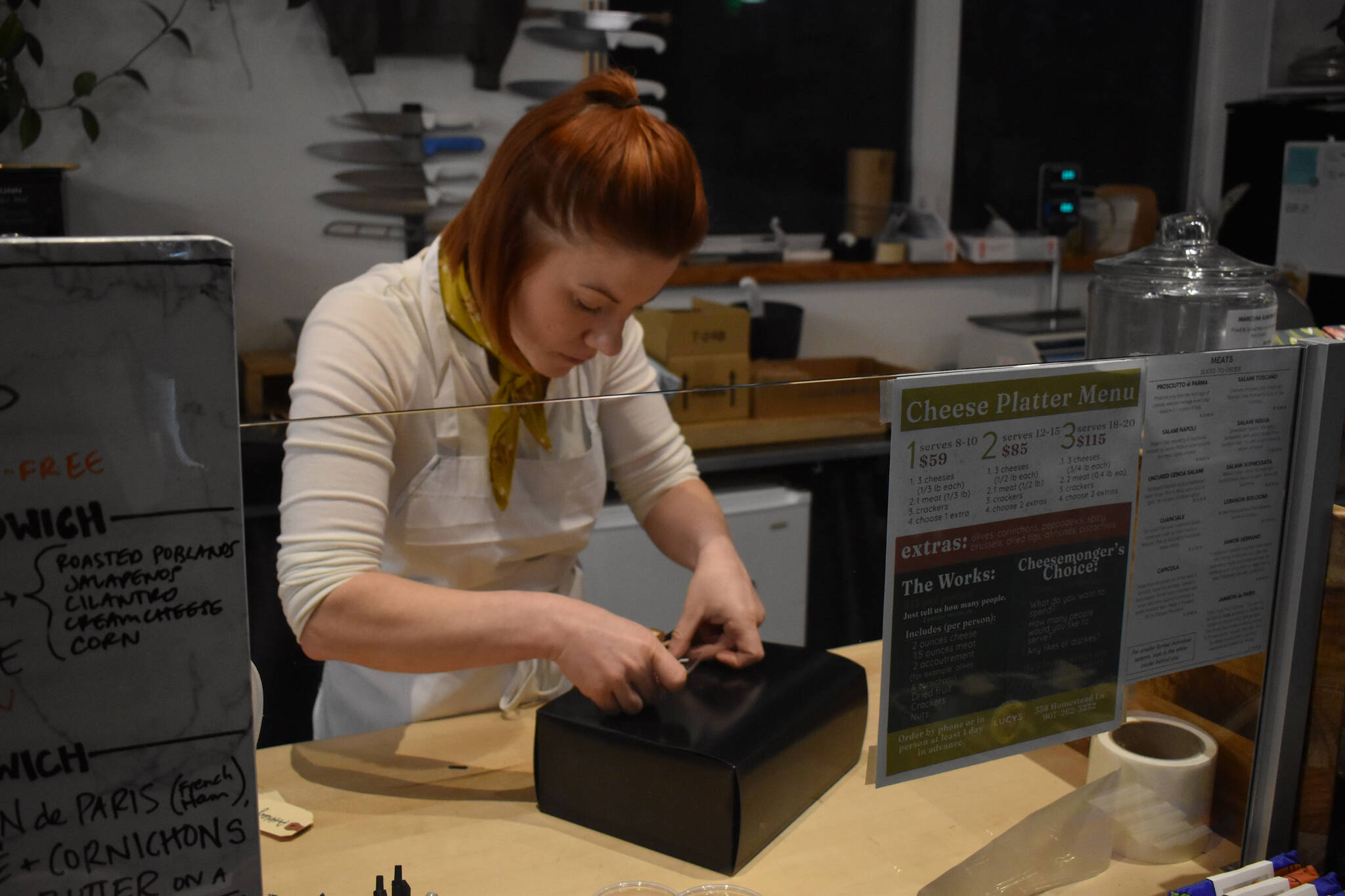 Kelsey Shields applies a “Lucy’s Market” sticker to a Cheese of the Month subscription box on Friday, Jan. 6, 2023 at Lucy’s Market in Soldotna, Alaska. (Jake Dye/Peninsula Clarion)