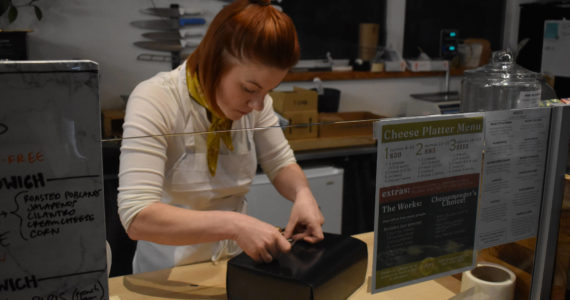 Kelsey Shields applies a “Lucy’s Market” sticker to a Cheese of the Month subscription box on Friday, Jan. 6, 2023 at Lucy’s Market in Soldotna, Alaska. (Jake Dye/Peninsula Clarion)