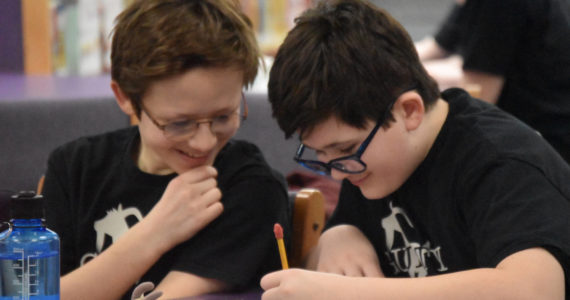 Luke Karpic and Oscar Marcou smile as they write their response to a question posed during Kenai Peninsula Borough School District Middle School Battle of the Books competition on Thursday, Feb. 9, 2023, at Kenai Middle School in Kenai, Alaska. (Jake Dye/Peninsula Clarion)