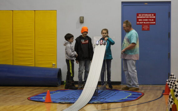 Photo by Delcenia Cosman/Homer News
Volunteer Mike Smith (right) supervises as Jack Roderick, Simon Smith, and Rox Shafer set their wood cars on the track in the Chapman School gym during the Snow Rondi Pinewood Derby on Saturday<ins>, March 4</ins> in Anchor Point<ins>,</ins> <ins>Alaska</ins>.