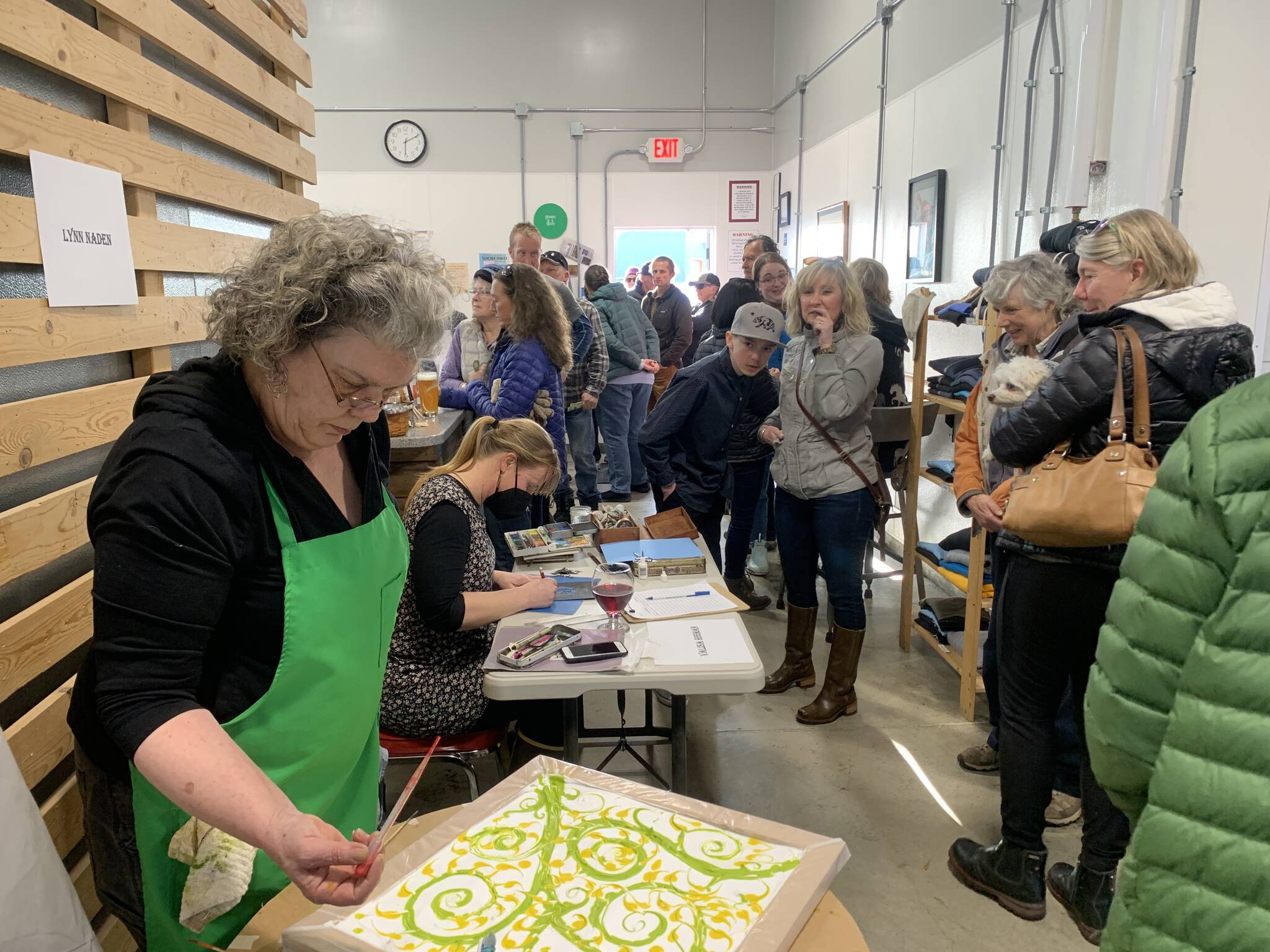 Lynn Naden (front left) paints scarves and Valisa Higman cuts paper during the Ptarmigan Arts scholarship fundraiser at Grace Ridge Brewing on Saturday. (Photo by Christina Whiting/Homer News)