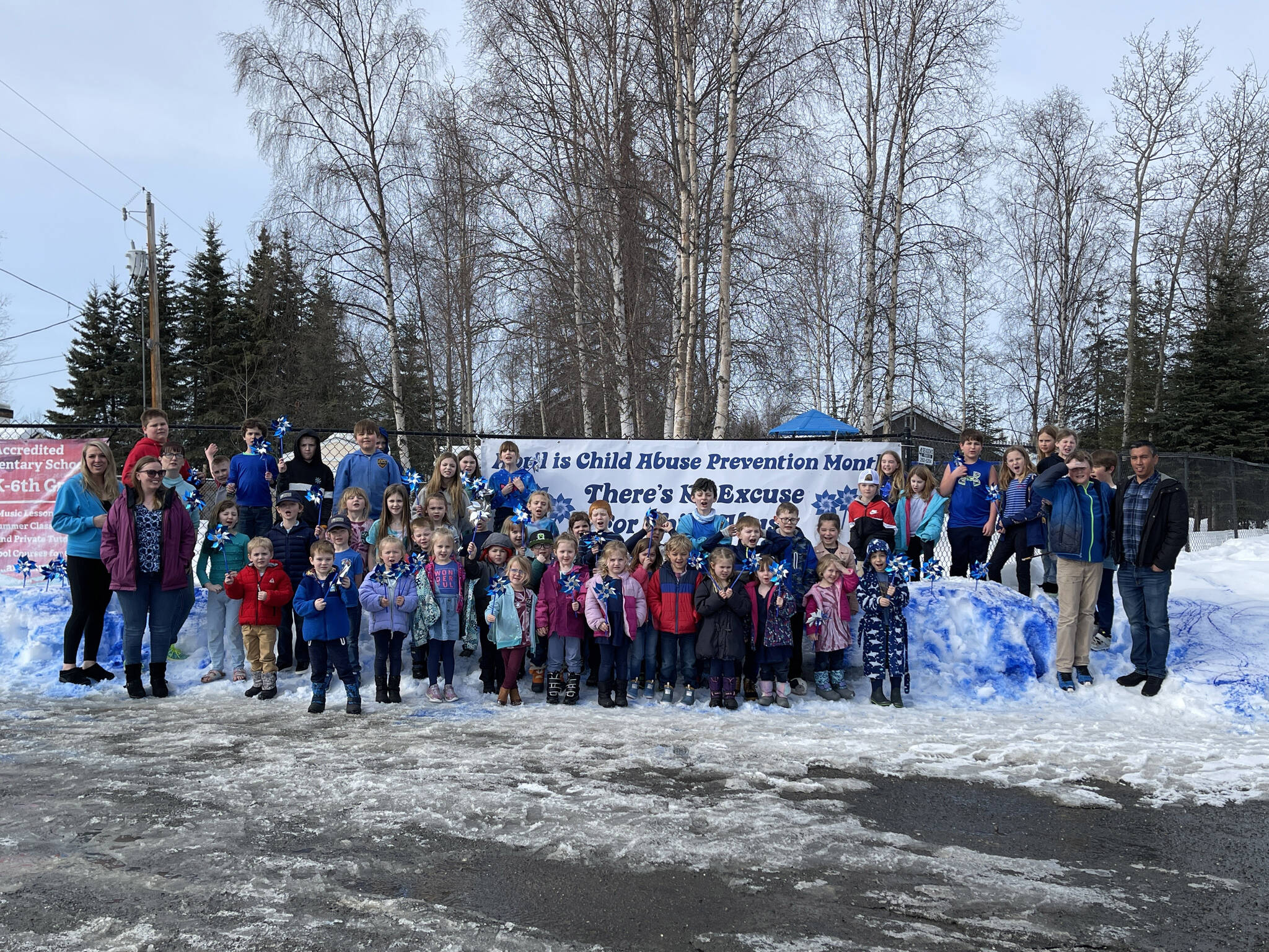 Students and teachers gather with pinwheels in hand in front of snow painted blue at The Study in Soldotna, Alaska, as they commemorate Go Blue Day on Friday, March 31, 2023, to kick off Child Abuse Prevention Month. (Jake Dye/Peninsula Clarion)