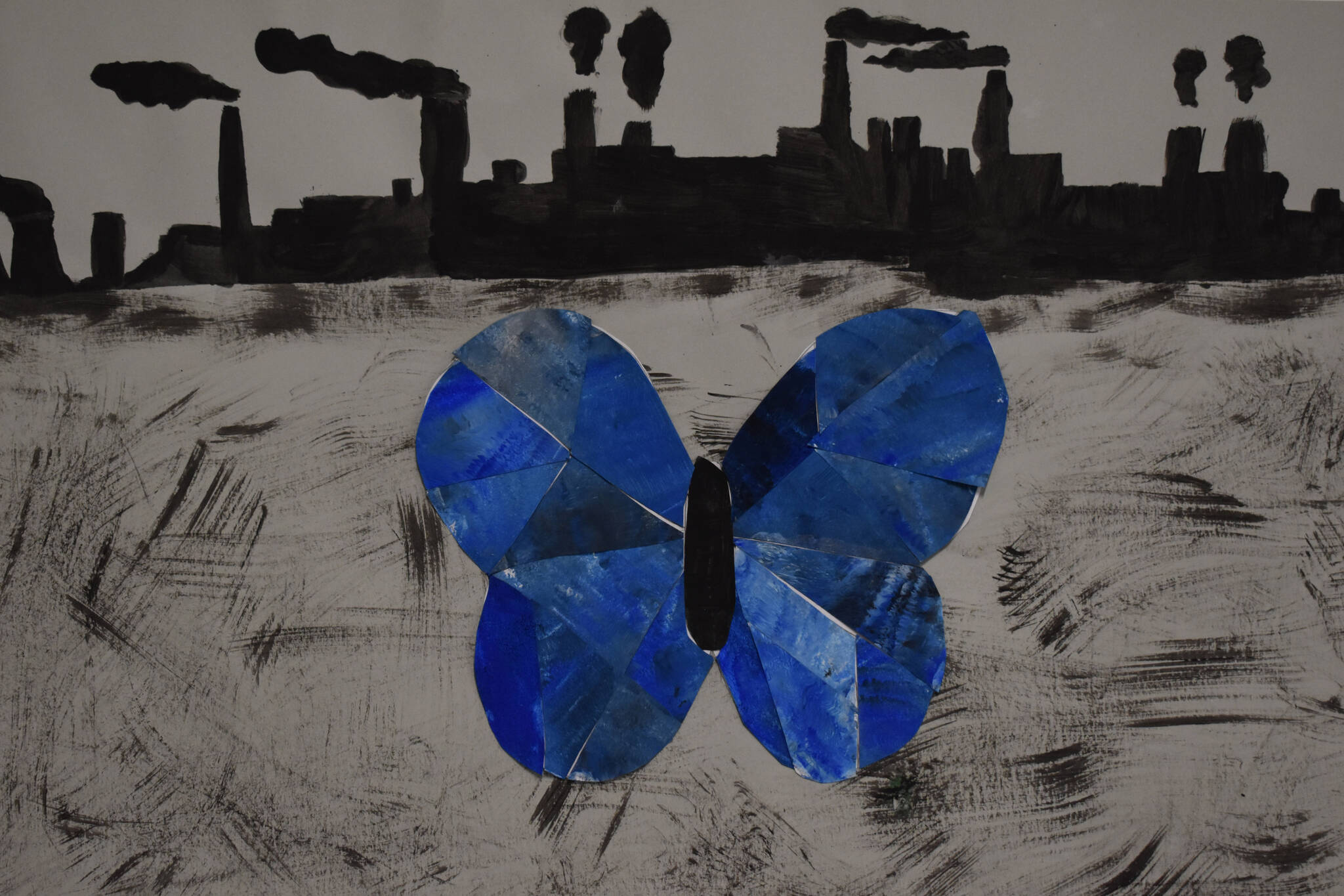 A blue butterfly is seen infront of a row of smokestacks in a painting hanging at the Kenai Art Center in Kenai, Alaska on Wednesday, April 5, 2023, in preparation for the debut of the 32nd Annual Kenai Peninsula Borough School District Visual Feast. (Jake Dye/Peninsula Clarion)