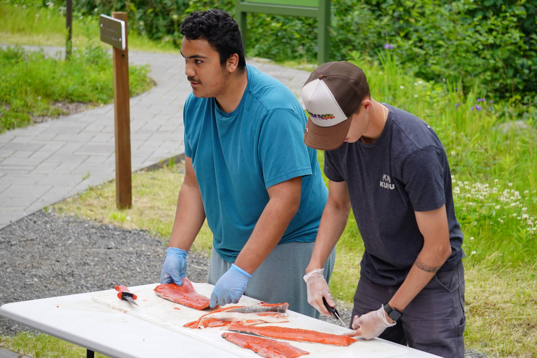 Marcus Wong and Ransom Hayes demonstrate slicing salmon fillets into strips during a smoked salmon demonstration, part of Fish Week 2023, on Wednesday, July 19, 2023, at the Kenai National Wildlife Refuge Visitor Center in Soldotna, Alaska. (Jake Dye/Peninsula Clarion)