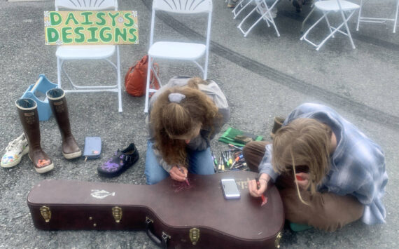 Daisy Walker (left) and her friend Leah Dunn paint a visiting musician's guitar case during the 2023 Solstice Festival on the Spit in Homer, Alaska. Photo by Christina Whiting