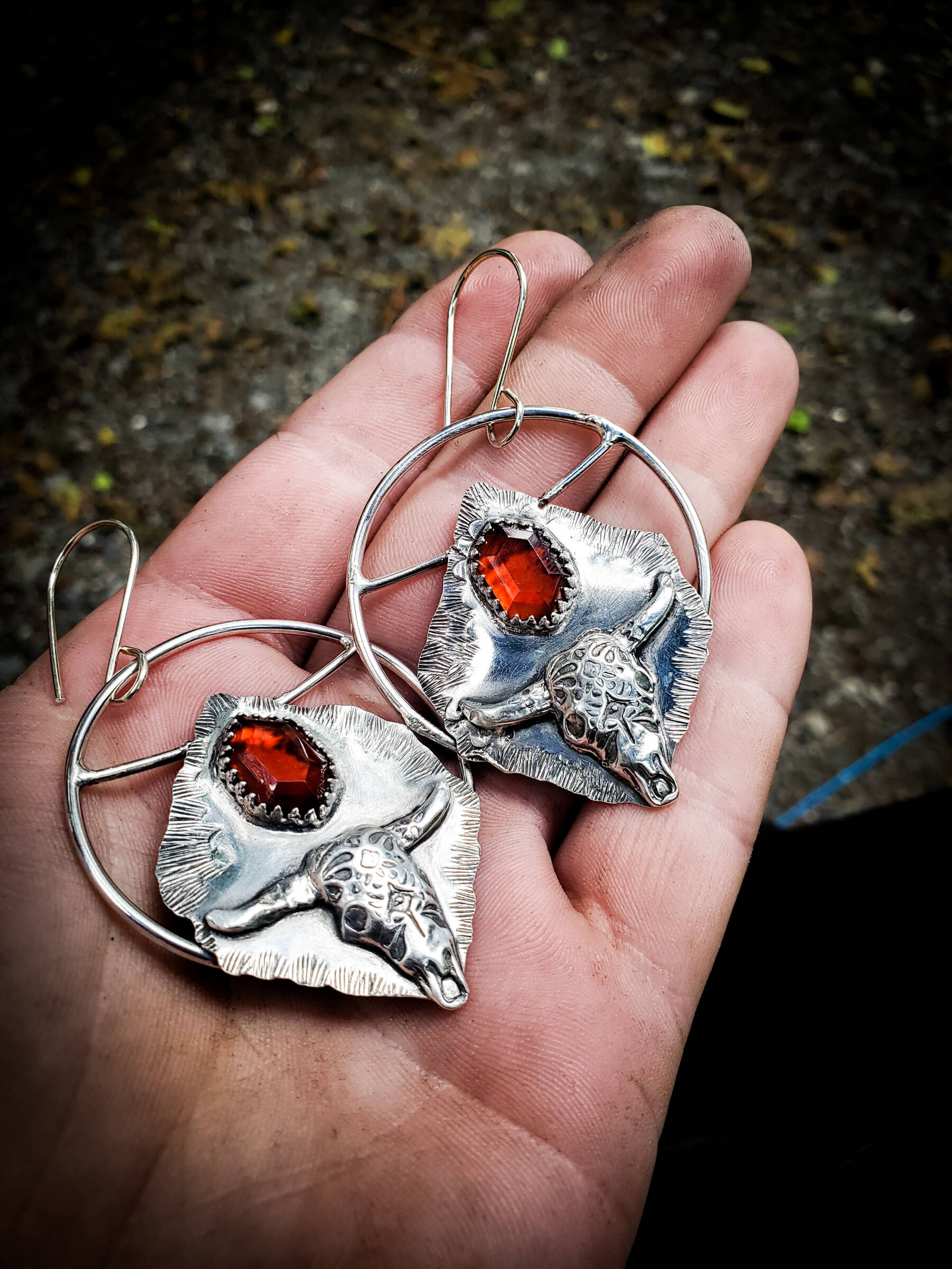 Hand-fabricated sterling silver hoops with silver clay cow skulls and two-step cut garnet cabochons were created by Homer artist Carley Conemac this past July. Photo provided