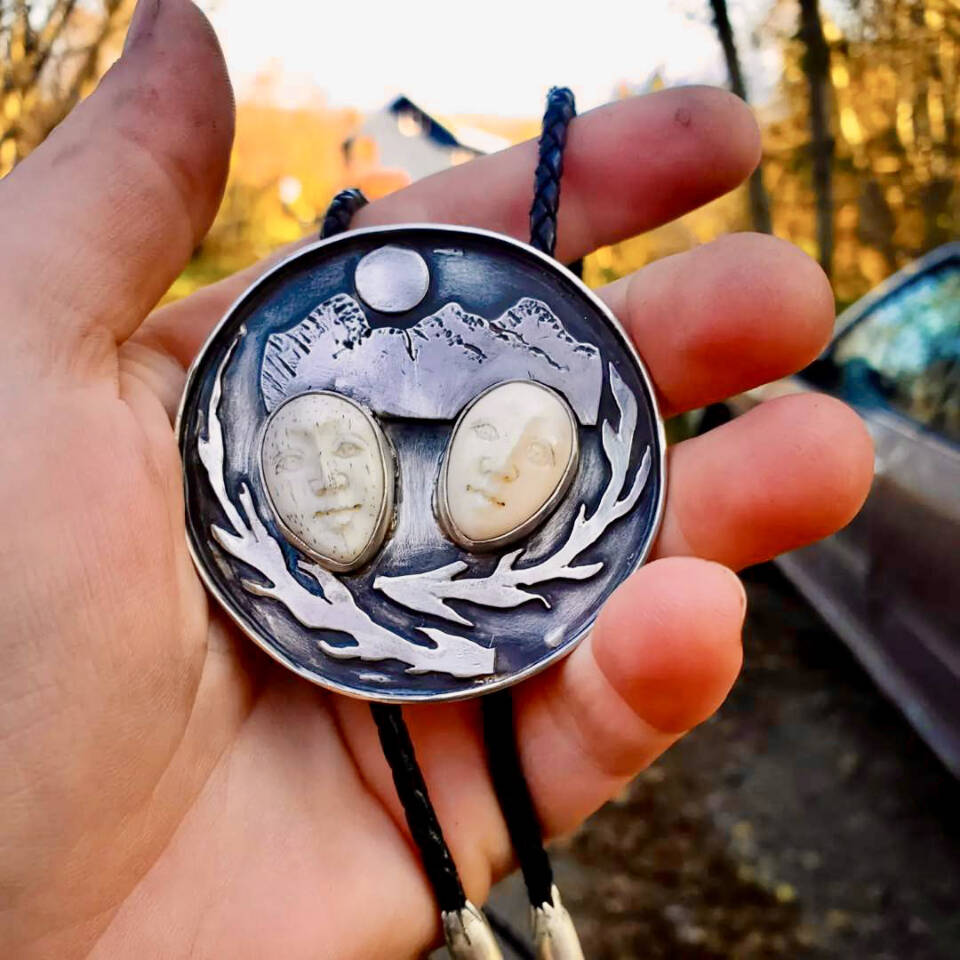 A bolo tie is hand-fabricated by Carley Conemac from sterling silver, with two water buffalo face carvings surrounded by branches and a mountainscape. Photo provided