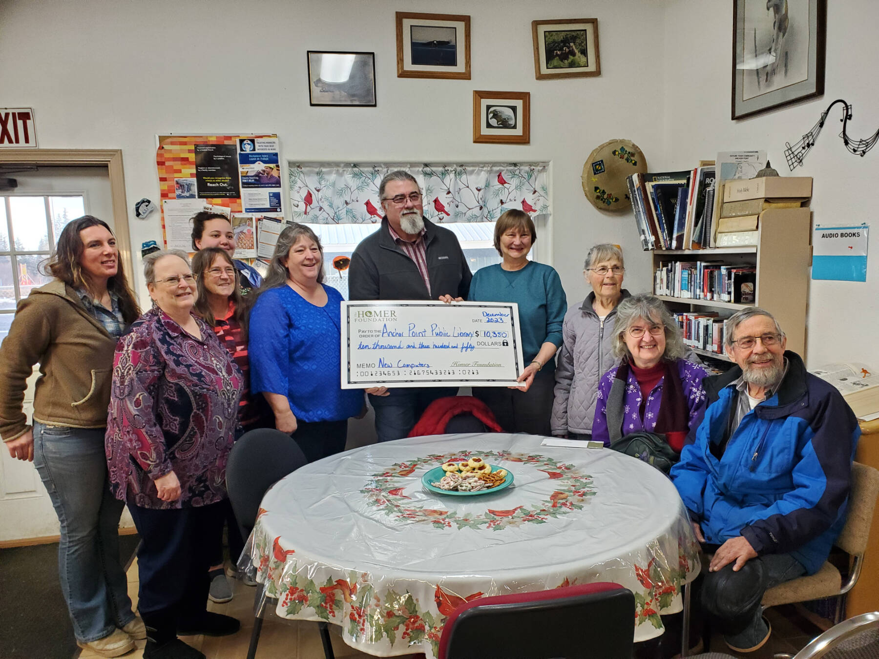 Homer Foundation executive director Mike Miller (center) presents a grant check to Anchor Point Public Library staff and board members (from left) Rachel Bice, Tressa Hidden Friend, Bobby Ness, Genevieve Winrod, Deanna Thomas, Mary Perry, Ann Bailey, Sandy Lettis and Don Bailey on Monday, Nov. 27, 2023 in Anchor Point, Alaska. (Delcenia Cosman/Homer News)