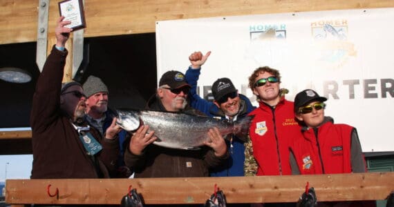 2023 tournament champion Gail Bilyeu, center, holds the winning fish during the Homer Winter King Salmon Tournament awards ceremony on Saturday, March 25, 2023, in Homer, Alaska. Pictured right are the 2022 and 2021 tournament champions, Weston and Andrew Marley. Photo by Delcenia Cosman