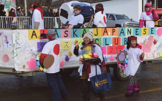 West Homer Elementary School Japanese Club instructor Megumi Beams (center), walking with the Alaska Japanese Club float, carries a cardboard Taiko drum and waves to the crowd at the 70th annual Homer Winter Carnival Parade on Pioneer Avenue on Saturday, Feb. 10, 2024 in Homer, Alaska. (Delcenia Cosman/Homer News)