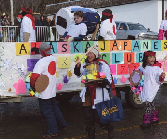 West Homer Elementary School Japanese Club instructor Megumi Beams (center), walking with the Alaska Japanese Club float, carries a cardboard Taiko drum and waves to the crowd at the 70th annual Homer Winter Carnival Parade on Pioneer Avenue on Saturday, Feb. 10, 2024 in Homer, Alaska. (Delcenia Cosman/Homer News)