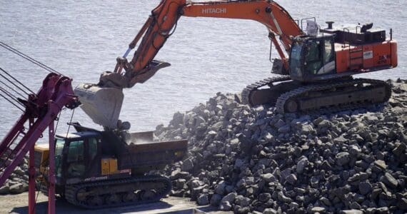 Armor rock from Sand Point is offloaded from a barge in the Kenai River in Kenai, Alaska, part of ongoing construction efforts for the Kenai River Bluff Stabilization Project on Wednesday, July 23, 2025. (Jake Dye/Peninsula Clarion)