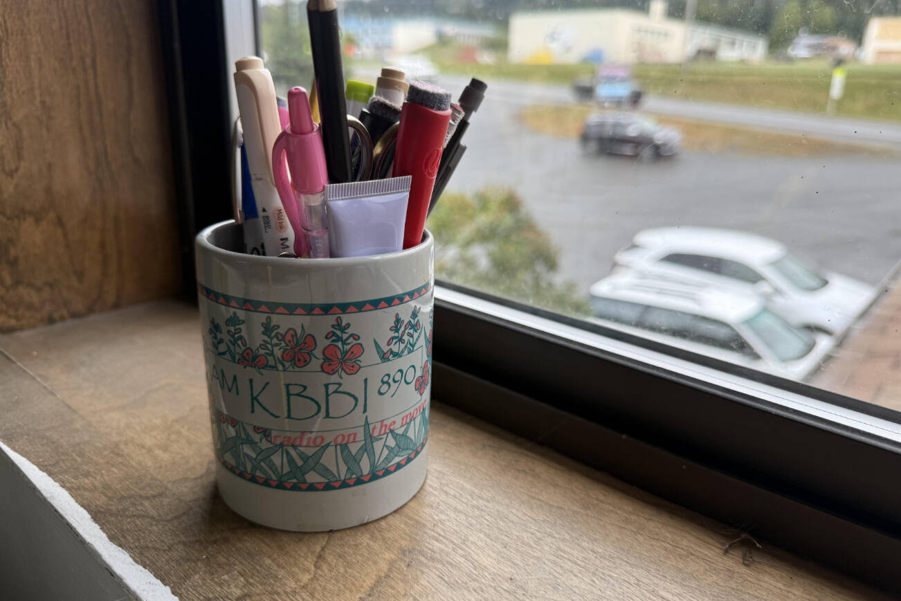 A vintage KBBI mug, repurposed and filled with various office supplies, rests in the Homer News office window on Friday, Aug. 8, 2025. (Chloe Pleznac/Homer News)
