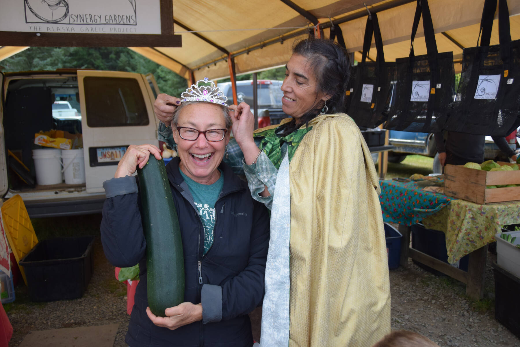 Christina Castellanos (right), 2024 Zucchini Queenie, crowns Synergy Gardens owner Lori Jenkins the new queen during the annual Zucchini Festival on Saturday, Aug. 23, 2025, at the Homer Farmers Market in Homer, Alaska. (Delcenia Cosman/Homer News)