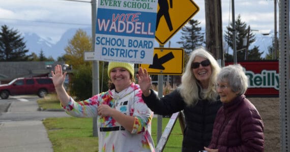 Ash-Lee Waddell (left), candidate for the District 9 seat on the Kenai Peninsula Borough School District Board of Education, holds a campaign sign and waves with supporters to passersby along the Sterling Highway in Homer, Alaska, on Election Day, Tuesday, Oct. 7, 2025. (Delcenia Cosman/Homer News)