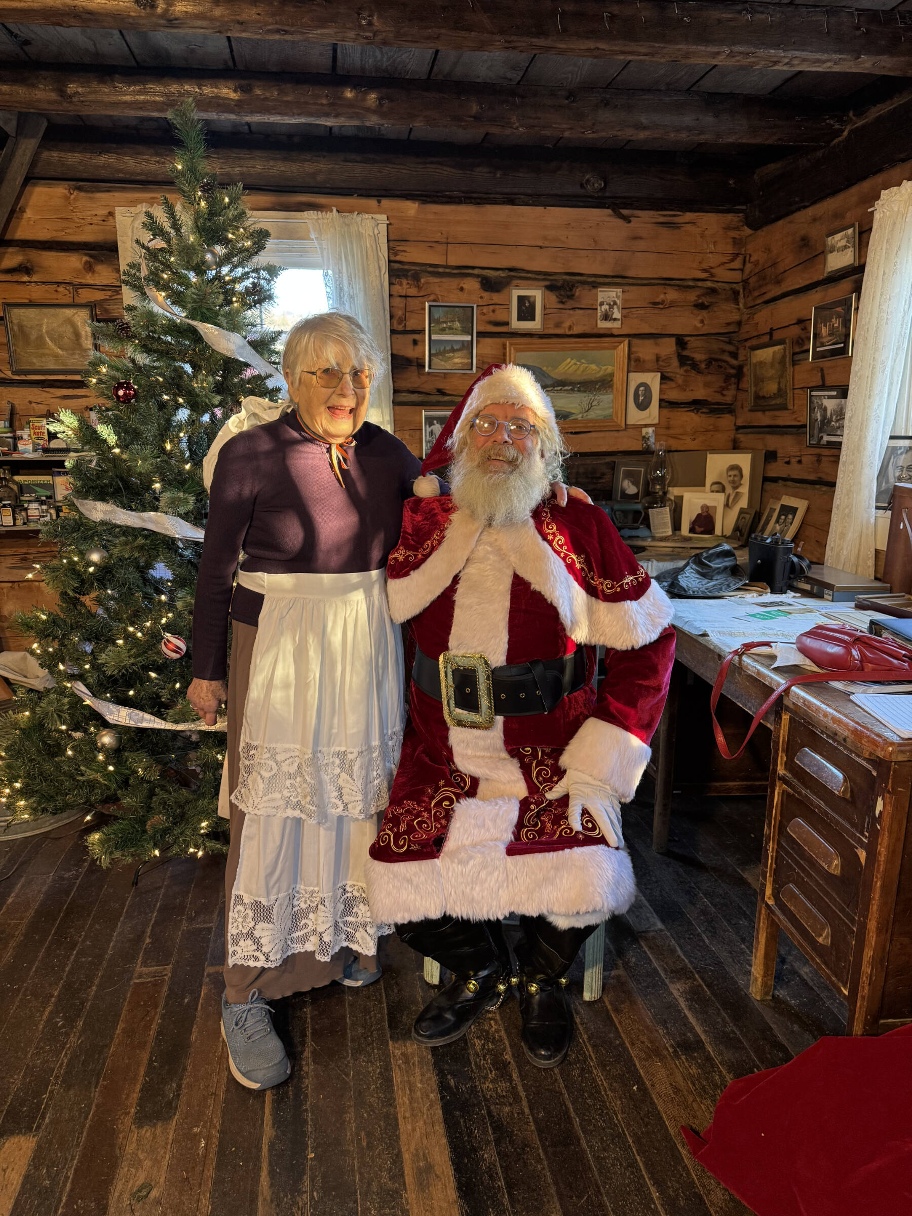 Milli Martin (left), the Homer Society of Natural History, Inc. Board Vice President, and Santa George Cutting III pose for a photo in the Pratt Museum Harrington Cabin on Saturday, Dec. 13, 2025, in Homer, Alaska. Photo provided by Whitney Harness