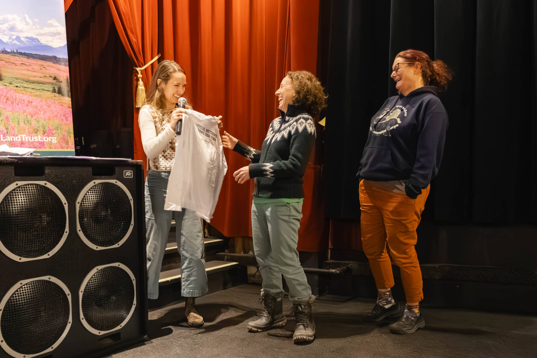 Kachemak Heritage Land Trust Communications & Development Manager Carson Chambers (left) presents gifts to Kachemak Bay National Estuarine Research Reserve Manager Katherine Schake (left) and Education Coordinator Ingrid Harrald as they receive the 2025 KHLT King Maker Award on Dec. 10, 2025, in Homer, Alaska. Photo courtesy Hayley Patton/KHLT