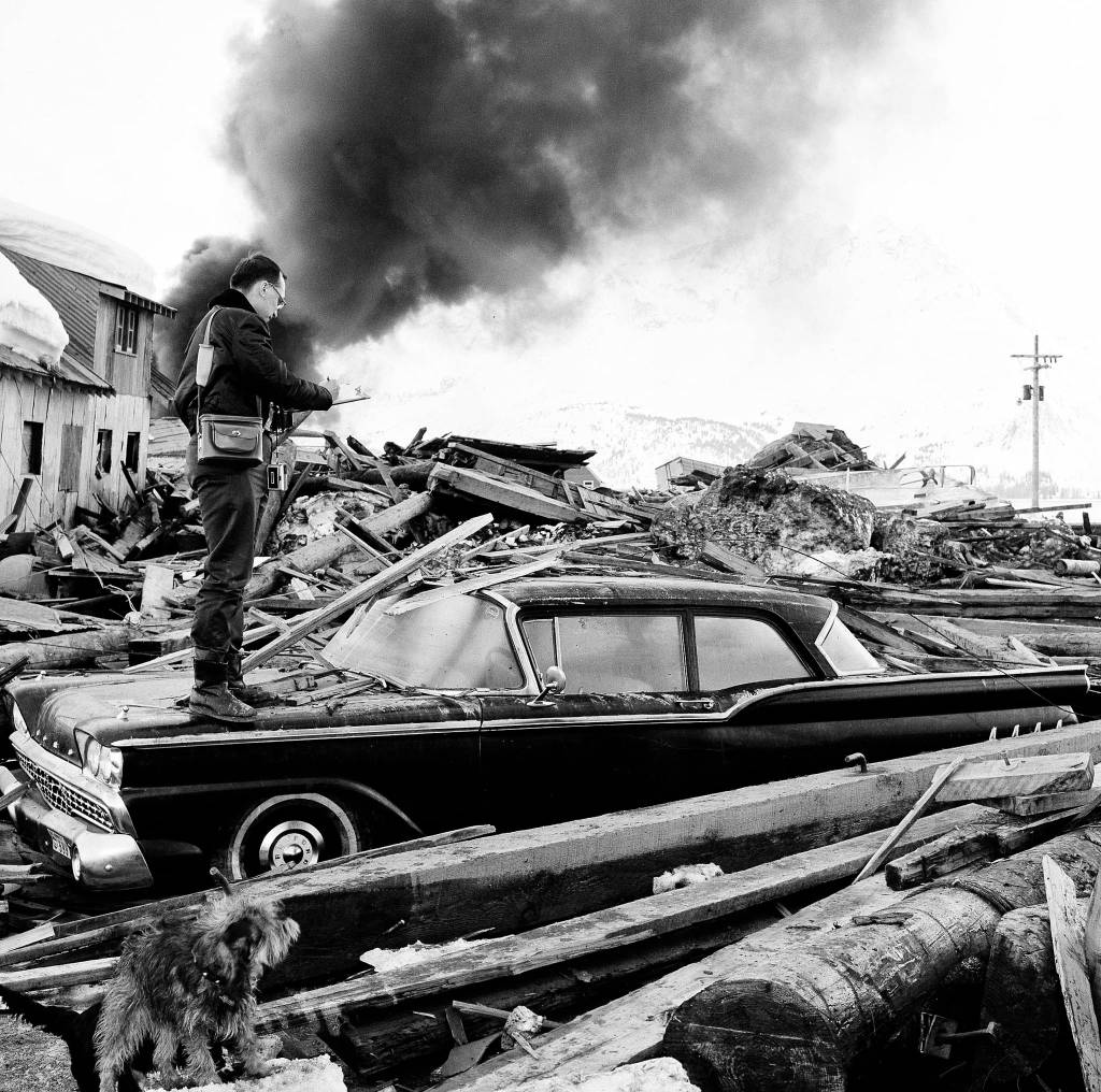 In this March 29, 1964 file photo, a photographer looks over wreckage as smoke rises in the background from burning oil storage tanks at Valdez on March 29, 1964. The city was hit hard by the earthquake that demolished some of Alaskas most picturesque and largest cities. North Americas largest earthquake rattled Alaska 54 years ago, killing 15 people and creating a tsunami that killed 124 more from Alaska to California. The magnitude 9.2 quake hit at 5:30 p.m. on Good Friday, turning soil beneath parts of Anchorage into jelly and collapsing buildings that were not engineered to withstand the force of colliding continental plates. (Associated Press file)