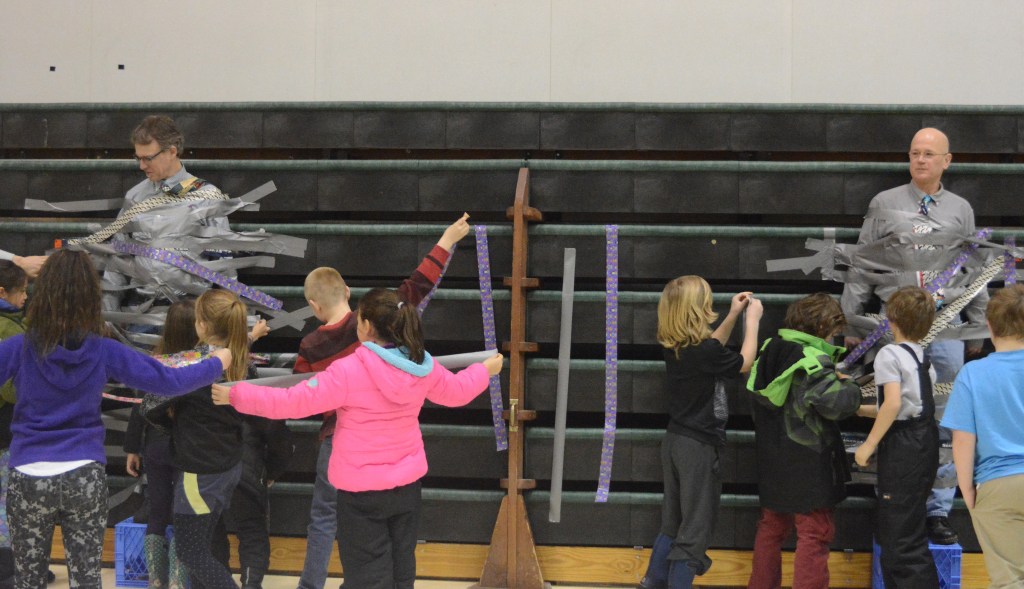 Students at West Homer Elementary School and Fireweed Academy duct tape their principals to the wall in the mutlipurpose room. At left is West Homer Elementary Principal Eric Waltenbaugh and at right is Fireweed Academy Principal Todd Hindman. The students got the reward of plastering duct tape across the principals for filling up a jar with tokens handed out when a student showed good behavior like being respectful and responsible.