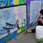 Kady Perry works on the Heath Street mural last Friday.  David Brame wrote the story told in the series of panels.