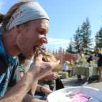 Synergy Gardens volunteer Tyler Schlieman takes a bite of pizza topped with local produce and edible flowers at Synergy Gardens' First Annual Great Garlic Scape Festival.