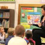 8:19 a.m.: Anne Love reads The Little Mouse, the Red Ripe Strawberry, and the Big Hungry Bear to her first grade class. Love gathered the kids on a rug with circles on it for each child to sit on and went over "Rug Rules," which include eye contact with teacher, listening, sitting cross-legged, hands in lap, and raises one's hand for permission to speak. She also told them that the class would keep count of the books they read as a class - 100 books earns a popcorn party and 200 books earns a pizza party.