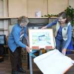 Cleo Webb and Sue Mauger unwrap the new watercolor painting of the Homer Public Library building, painted by local artist Jan Peyton, at the library building's 10th birthday celebration on Saturday, Sept. 17.