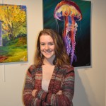 Breanna Brizendine poses with her painting, “Spotted Jellyfish,” at the opening of an exhibit of student art at Kachemak Bay Campus on Nov. 12. The nine artists were presenting work they’d created in Asia Freeman’s fall painting class.-Annie Rosenthal, Homer News