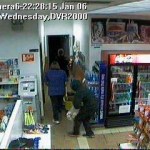 This screen capture of video footage taken at the Short Stop Tesoro gas station hows a man in a hoody standing behind two people in the store. The man holds a bag containing cash and cigarettes.-Photo provided, Homer Police Department