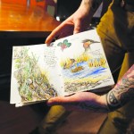 Sarah shows some pages from a journal project she’s working on. A tattoo artist, she did the ink on her left arm.-Photo by Michael Armstrong, Homer News