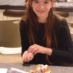 Mykayla Sarsfield, right, works on a graham-cracker house last Saturday for the Pratt Museum's annual Stocking Stuffer party. She wears a scrap-metal wreath she made earlier.-Photo by Michael Armstrong, Homer News