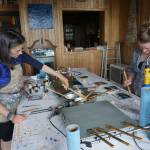 Carla Klinker-Cope., left, and Becca Bottebaum paint with encaustics in Ann-Margret Wimmerstedt&rsquo;s &ldquo;Wax. Wine & Wimmerstedt&rdquo;class held July 30, 2017 at Wimmerstedt&rsquo;s home. Wimmerstedt, far right, reaches for a propane torch. The torch is used to manipulate the wax by melting it and also to fuse the finished painting. &ldquo;Encaustic&rdquo; means &ldquo;to burn.&rdquo; (Photo by Michael Armstrong/Homer News)