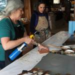 Ann-Margret Wimmerstedt heats a plywood board in preparation for painting with encaustics on July 30, 2017 at Wimmerstedt&rsquo;s home. &ldquo;Encaustics&rdquo; means &ldquo;to burn,&rdquo; and is the art technique of using pigmented hot wax to paint. Artist Carla Klinker-Cope, right, watches. (Photo by Michael Armstrong/Homer News)