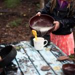 A Tiny Trees student plays in the outdoor play kitchen, pouring water from a bowl into a cup. (Photo by Scott Dickerson)