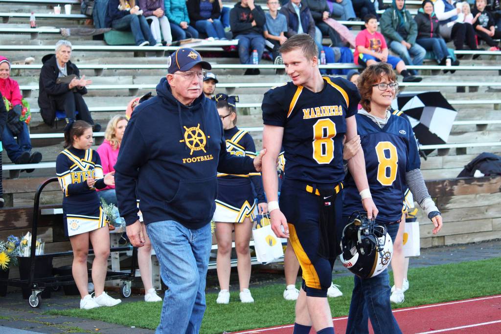 Homer senior and quarterback for the Mariners varsity football team Teddy Croft walks out to the field with his mother and grandfather during a senior night presentation during halftime of the team&rsquo;s game against the Head of the Bay Cougars on Friday, Sept. 29, 2017 at the high school field in Homer, Alaska. The Mariners beat the Cougars 53-0. (Photo by Megan Pacer/Homer News)