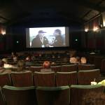 Homer residents watch Walter Love, head coach of the varsity football team, speak on the sidelines of the ASAA First National Bowl Series Division III Football State Championship game in Palmer on Saturday, Oct. 14, 2017 during a livestream event at the Homer Theatre. The Mariners lost to Barrow High School 20-14. (Photo by Megan Pacer/Homer News)