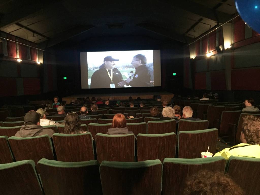 Homer residents watch Walter Love, head coach of the varsity football team, speak on the sidelines of the ASAA First National Bowl Series Division III Football State Championship game in Palmer on Saturday, Oct. 14, 2017 during a livestream event at the Homer Theatre. The Mariners lost to Barrow High School 20-14. (Photo by Megan Pacer/Homer News)