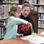Morgan Harness (left) performs a sound experiment under the guidance of her eigtht grade mentor, Caitlin Gamble, during a joint lesson Tuesday, Oct. 24, 2017 at Homer Middle School in Homer, Alaska. First grade students from Paul Banks Elementary were paired with the middle schoolers as they went through five different stations to teach them about sound. (Photo by Megan Pacer/Homer News)