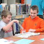 Colt Krueger (left) reacts to a sound experiment while working with Homer Middle School eighth grader Gabe Dash during a mentor lesson Tuesday, Oct. 24, 2017 at Homer Middle School in Homer, Alaska. Krueger and his fellow Paul Banks Elementary first grade classmates each paired up with a middle school student and completed five different stations in a new mentorship program between the schools. (Photo by Megan Pacer/Homer News)
