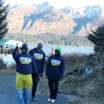 Human rights lawyer and Kenya native Chris Mburu takes a selfie with Kenny Daher of Project GRAD, center, and Kimani Nyambura, right, in front of the mountains Thursday, Nov. 16, 2017 in Port Graham, Alaska. Mburu, who started a foundation to put Kenyan children through school after being sponsored himself, gave presentations to several Kenai Peninsula schools this week along with Nyambura, one of the students who has been able to go to school thanks to the foundation. (Photo by Megan Pacer/Homer News)
