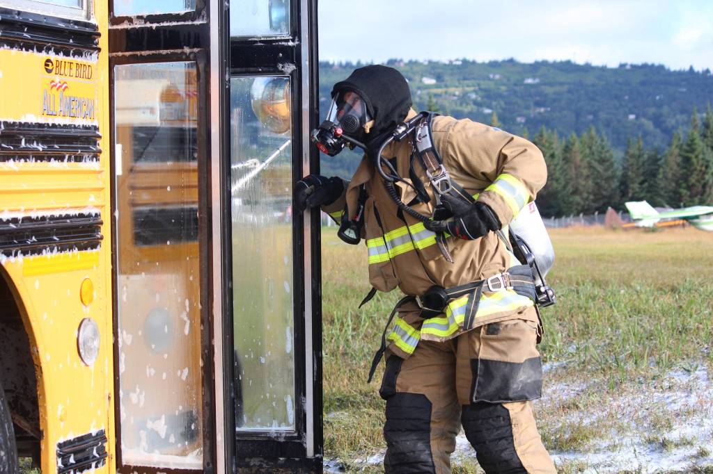 Firefighter Jesse Sherwood peers into a bus after spraying it down with foam during a simulated plane crash exercise Saturday, Aug. 19, 2017 at the Homer Airport in Homer, Alaska. He and members of several area emergency response agencies, along with airport personnel, completed the drill with the help of more than 20 volunteer &ldquo;victims.&rdquo; The drill is required every three years for the airport to stay in Federal Aviation Administration compliance. (Photo by Megan Pacer/Homer News)