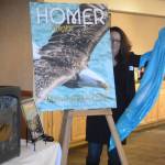 Homer Chamber of Commerce and Visitor Center board of director President Kari Ann Baker unveils the cover of the 2018 tourism and recreation guide at the chamber&rsquo;s annual meeting on Tuesday at the Best Western Bidarka Inn. The cover photo was taken by Collin Walker and picked in a contest held by the chamber. (Photo by Michael Armstrong, Homer News)