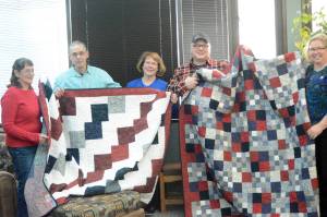 Jay Green, second from left, and Andrew Hodnik, second from right, hold up Quilts of Valor given to them and made by Dana Moore, far left, and Connie Isenhour, far right. The quilts are a project of Faith Friday Friends, a group at Faith Lutheran Church. Under the national program volutneers make quilts to honor service members and veterans touched by war. Green flew 196 combat missions in Vietnam as a U.S. Navy pilot from 1967-68 and Hodnik served in the U.S. Army as a combat engineer from 1989-93, including tours in Operation Desert Storm and Somalia. In the middle is Hodnik&rsquo;s mother, Dr. Vicky Hodnik. The quilts were presented at Hodnik&rsquo;s dental office on Feb. 6 in Homer, Alaska. (Photo by Michael Armstrong, Homer News)