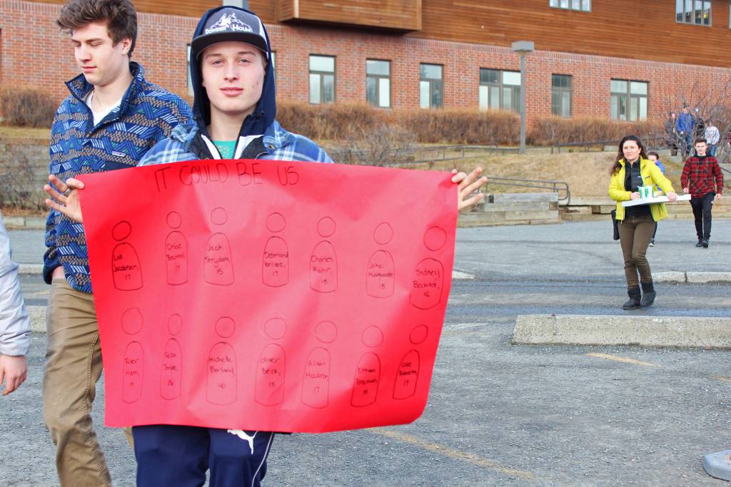 Freshman Charlie Tappan holds up a sign bearing the names and ages of the students killed in the Valentine&rsquo;s Day mass shooting in Parkland, Florida, as he and classmates walk out of Homer High School in a demonstration Wednesday, Feb. 21, 2018 in Homer, Alaska. (Photo by Megan Pacer/Homer News)
