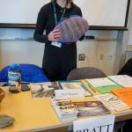 Pratt Museum education director Chessie Sharp holds a model chiton at the museum&rsquo;s table during the Kachemak Bay Campus College and Career Fair last Friday, March 30, 2018 in Homer, Alaska. About 400 students from 11 area schools as well as community members visited the annual event, said Kim Frost, KBC student and enrollment services coordinator. The Pratt has an opening for a student intern as well as several other full- and part-time jobs. (Photo by Michael Armstrong/Homer News)