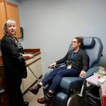 Homer Medical Center phlebotomist Peggie Inglis, left, demonstrates the new blood-draw chair with fellow phlebotomist Jessica James, right, at an open house for the expanded and remodeled clinic last Friday, March 30, 2018 on Bartlett Street in Homer, Alaska. (Photo by Michael Armstrong, Homer News)