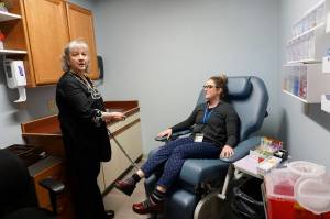 Homer Medical Center phlebotomist Peggie Inglis, left, demonstrates the new blood-draw chair with fellow phlebotomist Jessica James, right, at an open house for the expanded and remodeled clinic last Friday, March 30, 2018 on Bartlett Street in Homer, Alaska. (Photo by Michael Armstrong, Homer News)