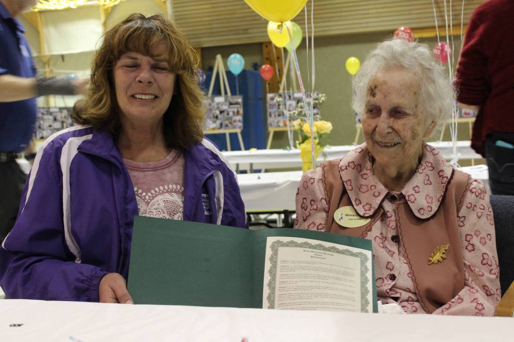 Kenai Peninsula Borough Assembly President Kelly Cooper, left, of Homer presents Wilma Gregory, right, of Homer with a borough proclamation naming Saturday Wilma Gregory Day in honor of Gregory&rsquo;s 100th birthday. Friends and family celebrated with Gregory at a birthday party held at McNeil Canyon Elementary School. (Photo by McKibben Jackinsky)