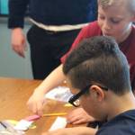 Fourth grader Kannon Hughes, background, helps sixth grader Ceiony Allen fold his seed tape, or a method of readying and storing seeds for later planting, on Tuesday, May 1, 2018 at Ninilchik School in Ninilchik, Alaska. Members of the Ninilchik chapter of the National FFA Organization visited the school to host educational sessions for Alaska Agriculture Day. (Photo by Megan Pacer/Homer News)
