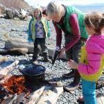 A May 2 outing for students in the Kenai Peninsula School District&rsquo;s Wilderness Explorers program in Homer is an opportunity for volunteer Tania Spurkland (center) to teach Estelle Velsko (left) and Allie Barker (right) how to prepare stinging nettles over a campfire. (Photo by McKibben Jackinsky)